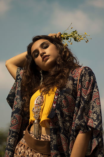 A fashionable South Asian woman with flowers poses stylishly under a blue sky. HD phone wallpaper