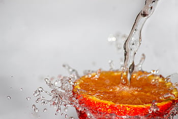 A high-speed capture of water splashing onto a juicy orange slice, creating a refreshing visual. HD wallpaper