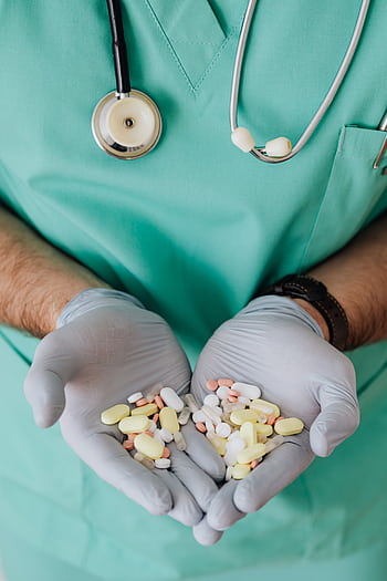 Medical professional in scrubs holds various pills, symbolizing healthcare and medicine. HD phone wallpaper