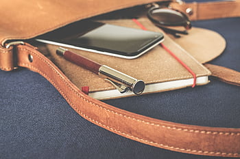 Stylish leather bag with a fountain pen, smart, and notebook on display. HD wallpaper