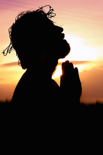 A silhouette of a man praying at sunset, wearing a crown of thorns, symbolizing faith and hope. HD phone wallpaper