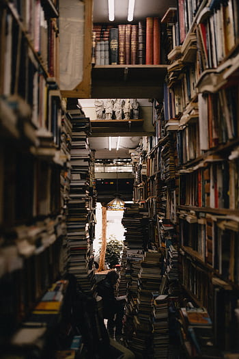 A densely packed library aisle with numerous stacks of books creating a warm and inviting atmosphere. HD phone wallpaper