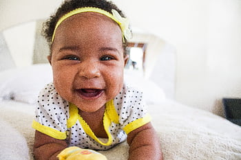 Cheerful baby girl in a polka dot outfit with a big smile on a bed indoors. HD wallpaper