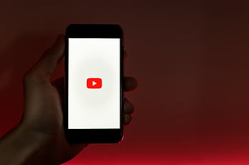 A hand holding a smart displaying the YouTube app against a red background. HD wallpaper
