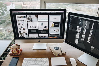 A well-organized workspace showcasing dual Apple iMacs on a wooden desk ideal for design and productivity. HD wallpaper