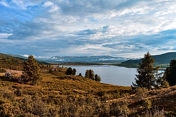 que landscape featuring a lake surrounded by mountains and trees under a cloudy sky. HD wallpaper