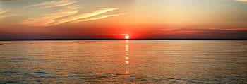 Vibrant sunset over a calm ocean with reflecting water and colorful sky. HD wallpaper