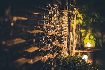 A serene and illuminated garden waterfall captured at night, featuring cascading water over bricks and soft ambient lighting. HD wallpaper