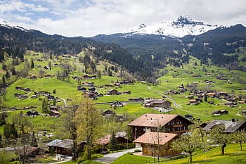 Charming village surrounded by lush green hills and snowy mountains in Interlaken, Switzerland. HD wallpaper