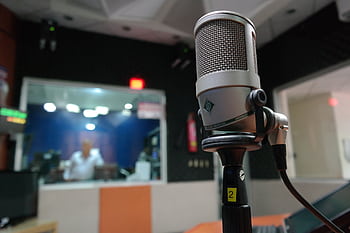 Close-up of a micro in a recording studio with a blurred sound engineer in the background. HD wallpaper