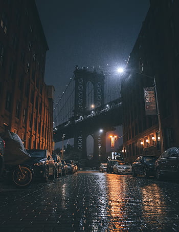 Night view of the Manhattan Bridge with wet cobblestone streets in NYC, showcasing urban architecture. HD phone wallpaper