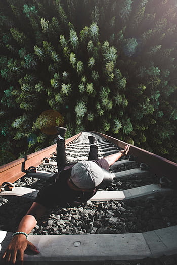 A man poses daringly over train tracks with a forest view. HD phone wallpaper