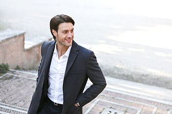 Confident man in a suit smiling while walking outdoors, showcasing fashion and style. HD wallpaper