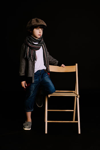 A fashionable young boy posing with a chair in a studio on a dark background. HD phone wallpaper