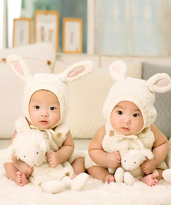 Twin babies wearing cute bunny outfits with plush toys indoors. HD phone wallpaper