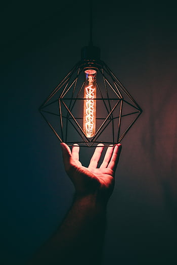 Conceptual of a hand holding a geometric pendant light bulb, symbolizing creative energy. HD phone wallpaper