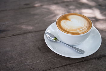 A close-up of a creamy latte with heart latte art on a wooden table, perfect for morning caffeine lovers. HD wallpaper