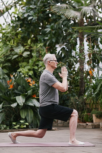 A senior man gracefully performs a yoga pose in a lush botanical garden, embodying mindfulness and well-being. HD phone wallpaper
