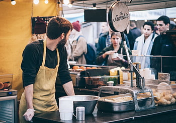 Dynamic scene of a street food vendor working in a busy market, engaging with diverse customers. HD wallpaper