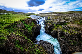 Captivating waterfall flowing through rocky terrain and vibrant green moss in a remote nature setting. HD wallpaper