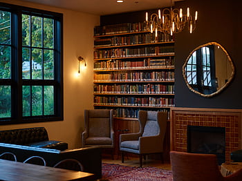 Warm and cozy library living room featuring armchairs, bookshelves, and a fireplace, perfect for reading and relaxation. HD wallpaper