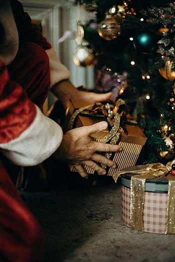 Santa Claus placing gifts under a beautifully decorated Christmas tree, capturing the holiday spirit. HD phone wallpaper