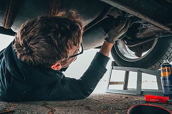 Mechanic skillfully repairing car undercarriage in outdoor setting with tools. HD wallpaper