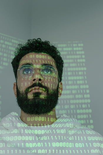 A bearded man with eyeglasses analyzing data in a digital environment with green binary code projections. HD phone wallpaper