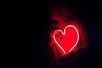 Silhouette of a person with a glowing red neon heart in the dark, symbolizing love. HD wallpaper