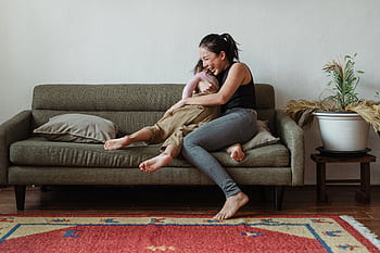 A happy mother and daughter laughing together on a cozy living room sofa. HD wallpaper
