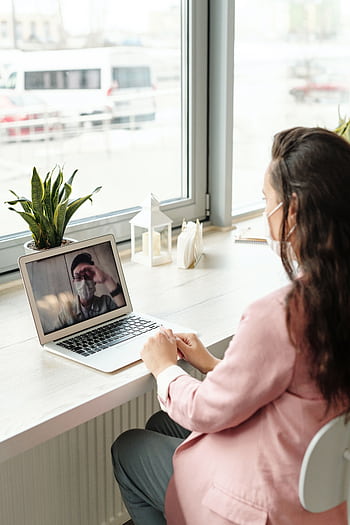 A woman wearing a face mask participates in a video call from her home office, showcasing remote work during the pandemic. HD phone wallpaper