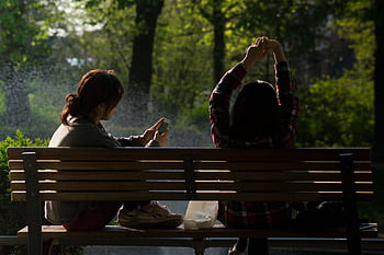 Two women sitting on a park bench enjoying leisure time with a smart. HD wallpaper