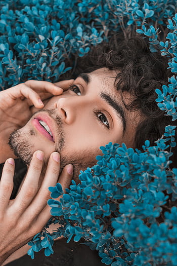 Close-up portrait of a man surrounded by vibrant blue flowers, expressing a serene mood. HD phone wallpaper
