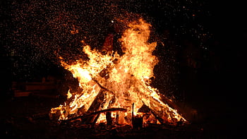 A large bonfire blazing at night with embers and sparks flying into the dark sky. HD wallpaper