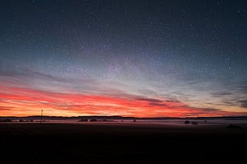 Captivating view of a starry sky blending with a vibrant sunset over a tranquil field. HD wallpaper