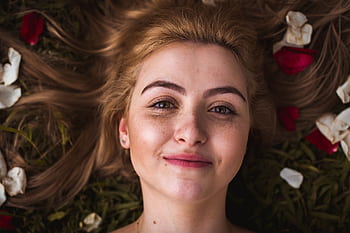 Portrait of a smiling young woman with rose petals in her hair, lying on grass outdoors. HD wallpaper