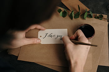 Person crafting a beautiful 'I love you' card with calligraphy, featuring eucalyptus and ink. HD wallpaper