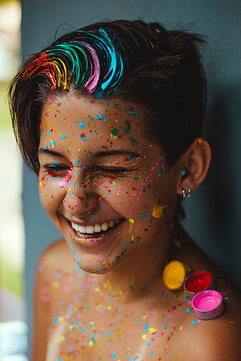 Smiling woman with vibrant face paint and colorful confetti, celebrating happiness and creativity. HD phone wallpaper