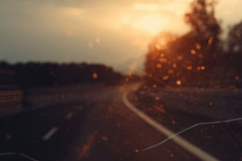 Blurry view of a road and sunset seen through a car windshield, creating a dreamy effect. HD wallpaper