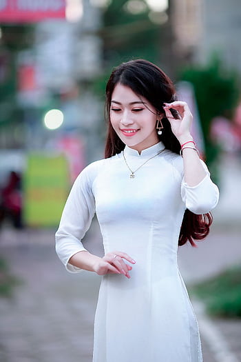 A woman in a white Ao Dai poses gracefully outdoors, showcasing traditional Vietnamese fashion. HD phone wallpaper