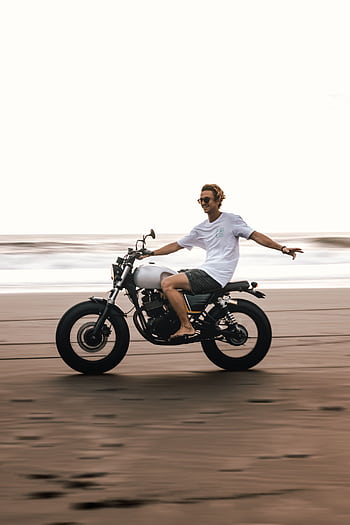 Young man enjoying a care motorcycle ride on a Bali beach, showcasing leisure and adventure. HD phone wallpaper