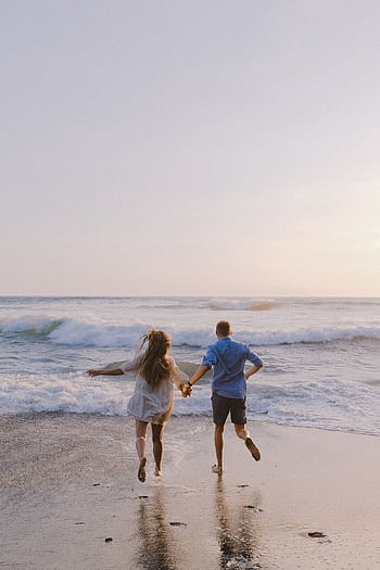 A couple holding hands, running barefoot on a beach at sunset, symbolizing romance and dom. HD phone wallpaper