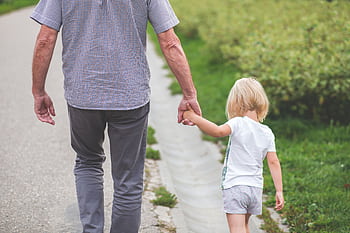 A grandparent holds hands with a child, walking on a path in a park, symbolizing family and togetherness. HD wallpaper