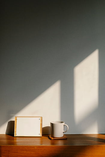 A simple, sunlit scene with a mug and empty frame on a wooden surface, casting long shadows. HD phone wallpaper