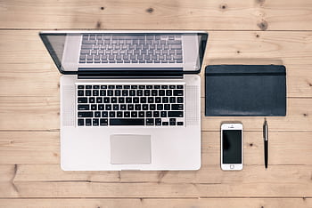 Top view of a tidy workspace featuring a laptop, smart, notebook, and pen on a wooden desk. HD wallpaper