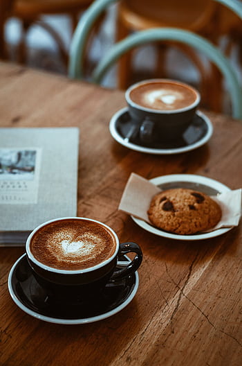 Cozy cafe setup with cappuccinos and a chocolate chip cookie on a rustic wooden table. HD phone wallpaper