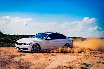 White luxury car drifting on a dirt road, creating a dramatic dust cloud under a blue sky. HD wallpaper