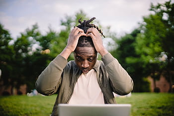Young man with dreadlocks appears stressed while working on a laptop outdoors. HD wallpaper