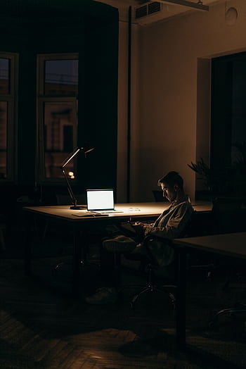 A lone man working on a laptop under dim lighting in a quiet office at night. HD phone wallpaper