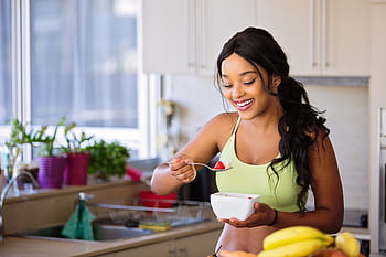 Smiling woman eating a nutritious fruit bowl in a bright kitchen setting. HD wallpaper